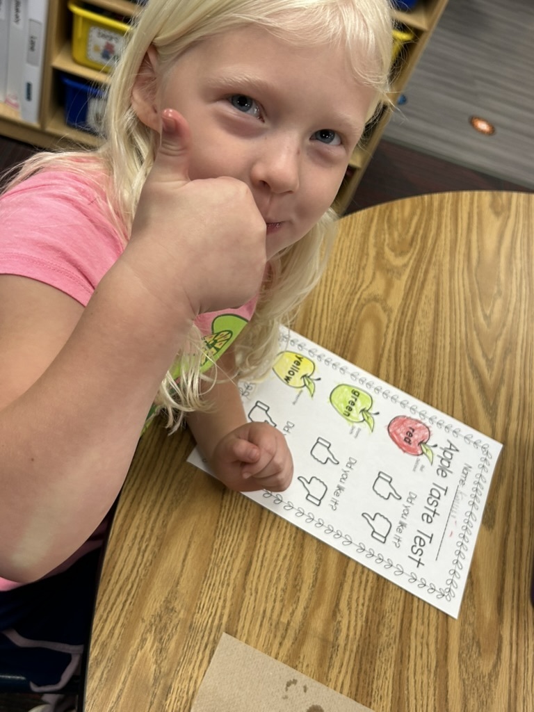 Girl holding her thumb up in front of a paper that says Apple Taste Test.