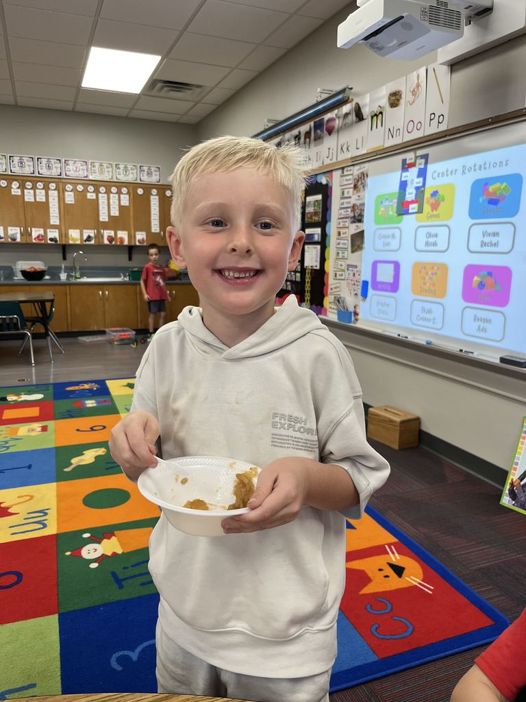 Boy with a white sweatshirt standing and smiling while holding a white bowl filled with apple sauce.
