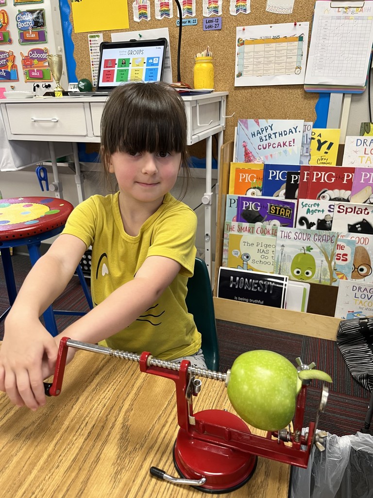 Girl with a yellow shirt holding a handle to an apple peeler that is peeling a green apple.
