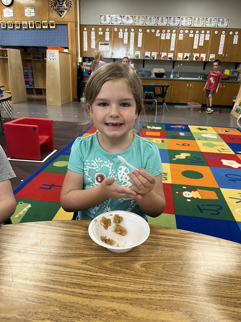 Girl sitting at a table smiling with applesauce sitting on the table in a white bowl.