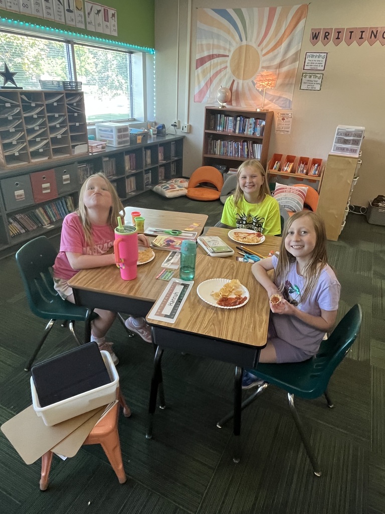 Group of students sitting in a classroom at desks with water bottles and plates filled with chips and salsa on the plates.
