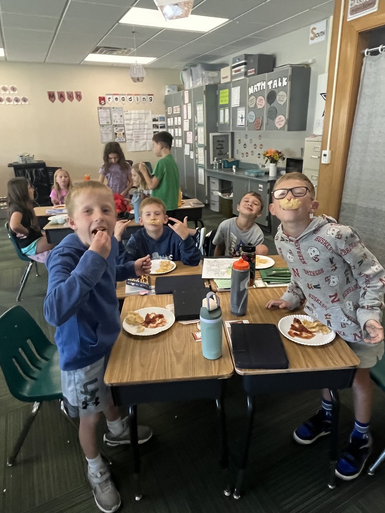 Group of students sitting in a classroom at desks with water bottles and plates filled with chips and salsa on the plates.