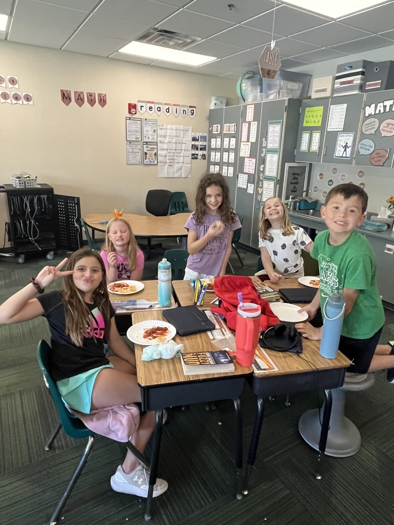 Group of students sitting in a classroom at desks with water bottles and plates filled with chips and salsa on the plates.