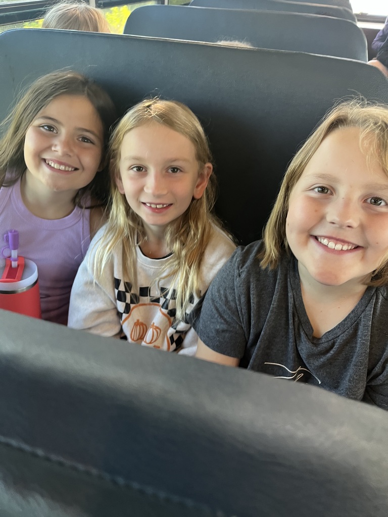 Three girls sitting on a bus in a seat while smiling.
