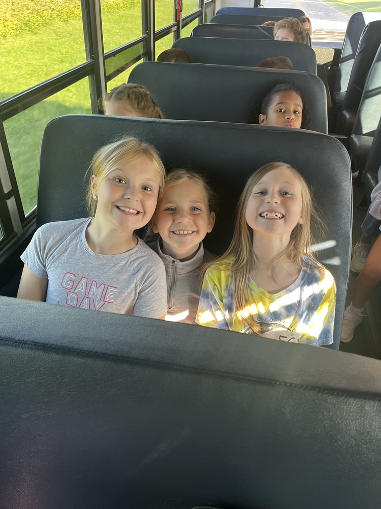 Three girls sitting on a bus in a seat while smiling.