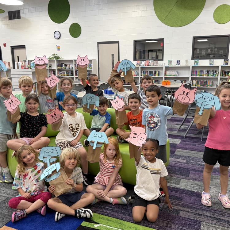 A class of kindergartners holding up Elephant or Piggie puppets. 