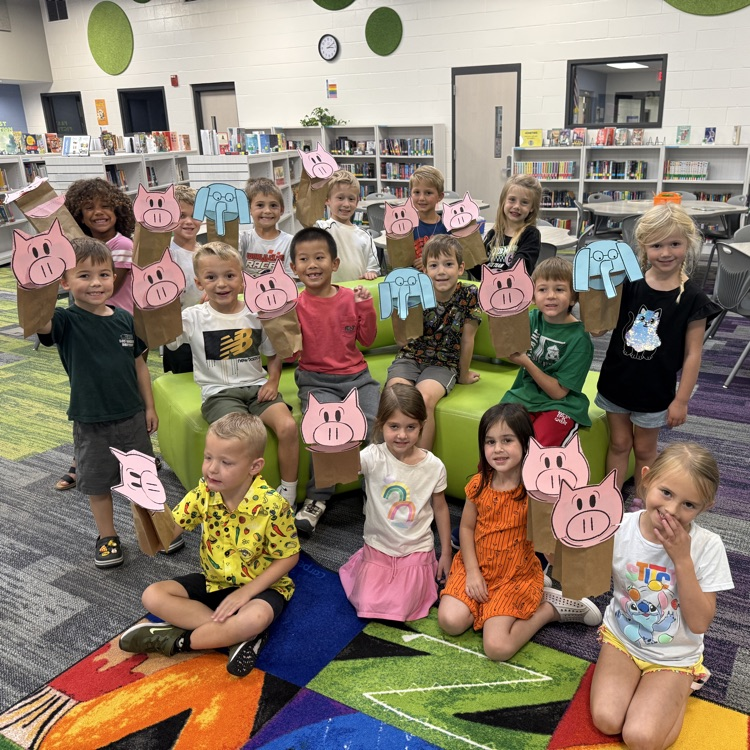 A class of kindergartners holding up Elephant or Piggie puppets. 