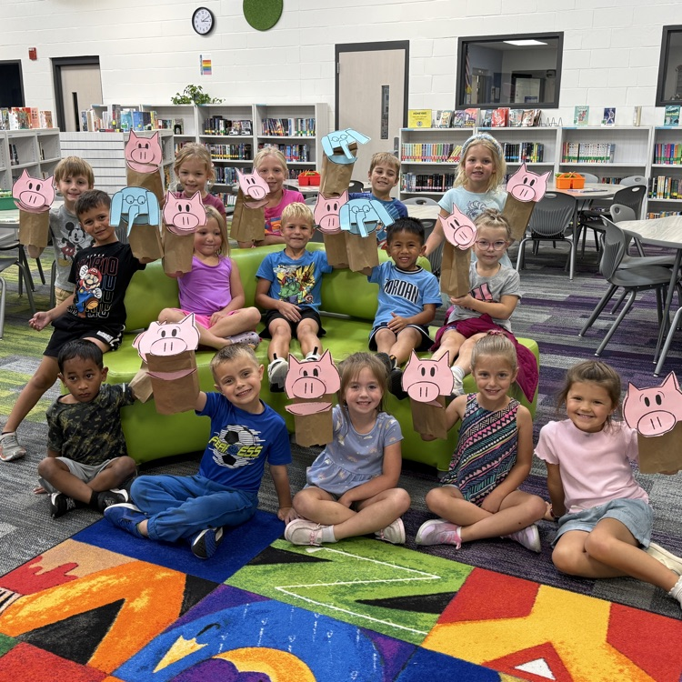 A class of kindergartners holding up Elephant or Piggie puppets. 