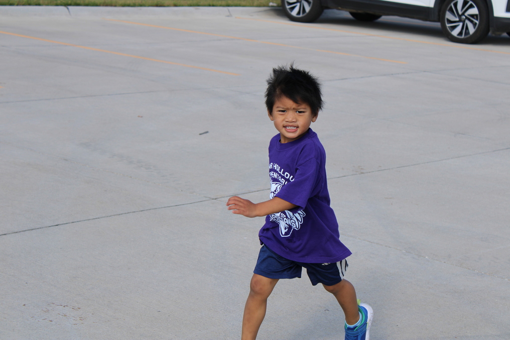 A preschool student flashes a smile as he runs around the track. 