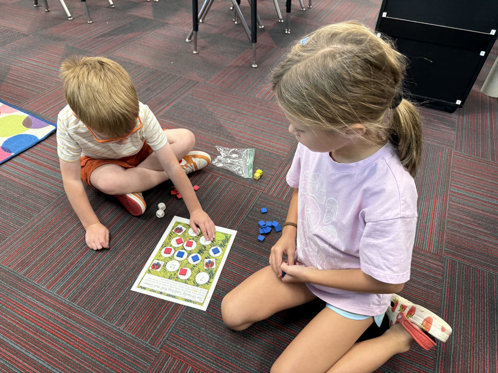 A boy wearing shorts sitting on the ground with a girl while playing a game with blue and red tiles.