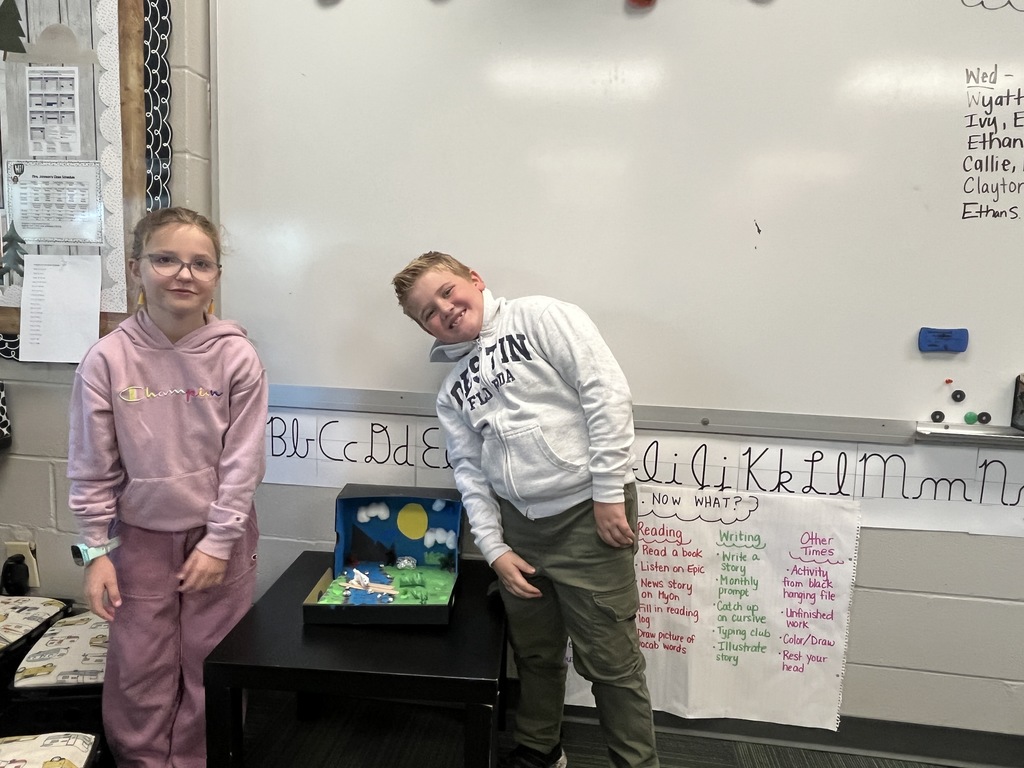 Boy and girl smiling standing next to a black shoe box with a diorama of an animal made with art supplies inside.