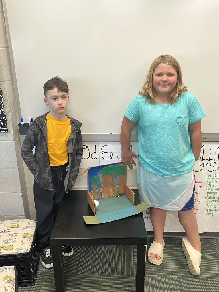 Boy and girl standing next to a brown shoe box with the inside painted with trees.