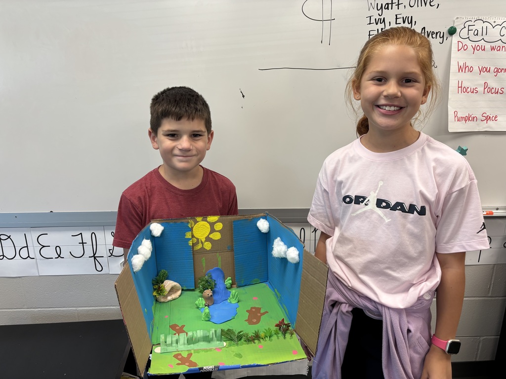 Boy and girl holding a decorated box with a diorama of animals inside the box.
