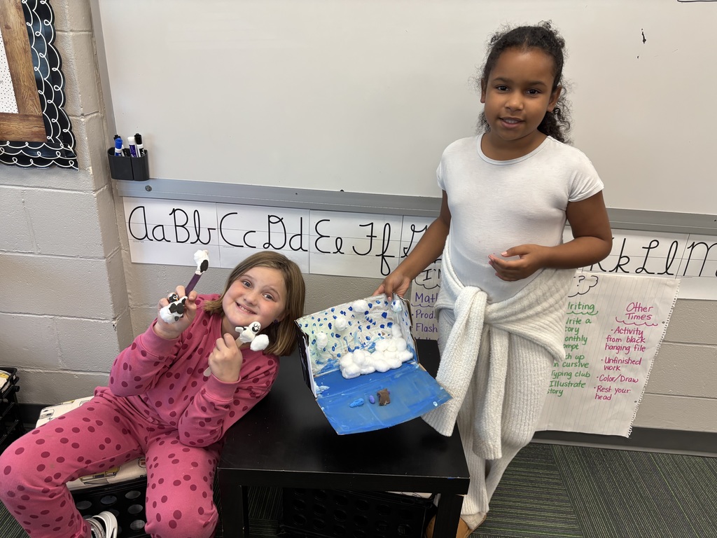 Two girls holding a decorated box with a diorama of animals inside the box.