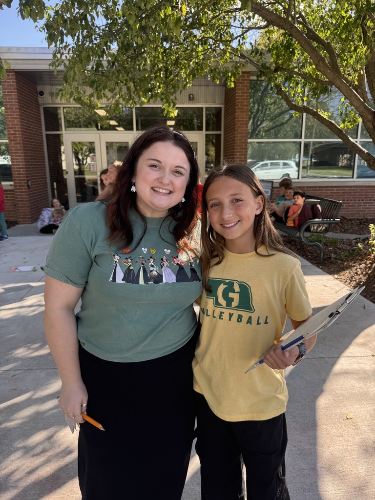 Girl and her teacher smiling outside in front of a school.