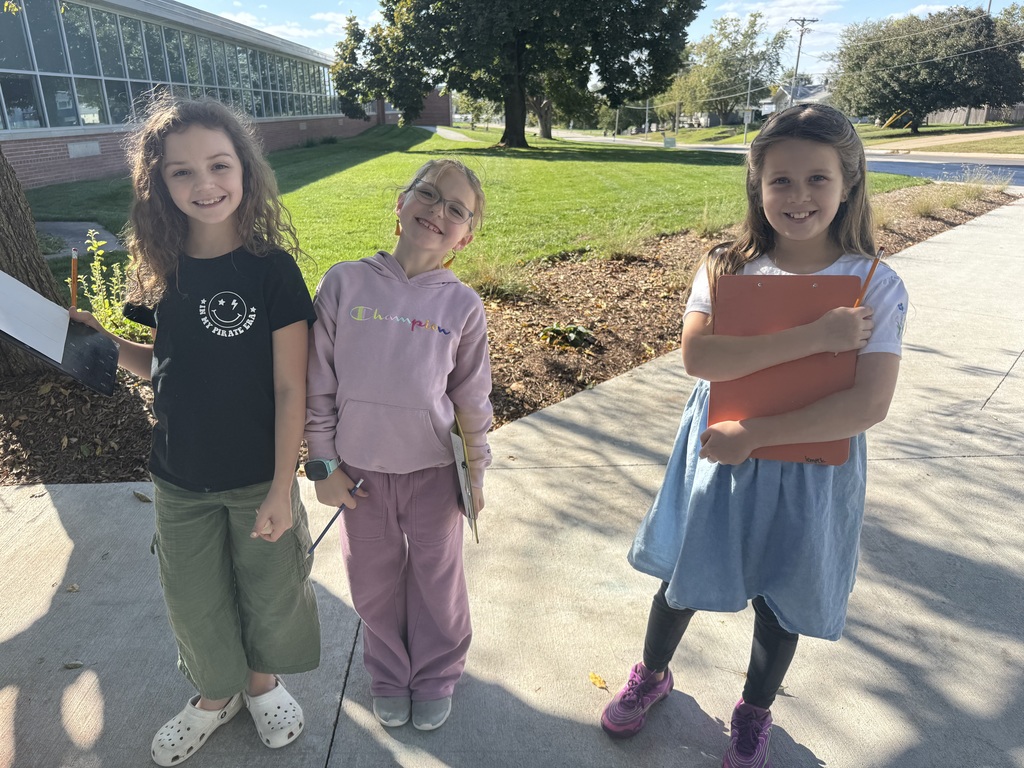 Three girls standing outside on cement with clipboards and papers in their hands.