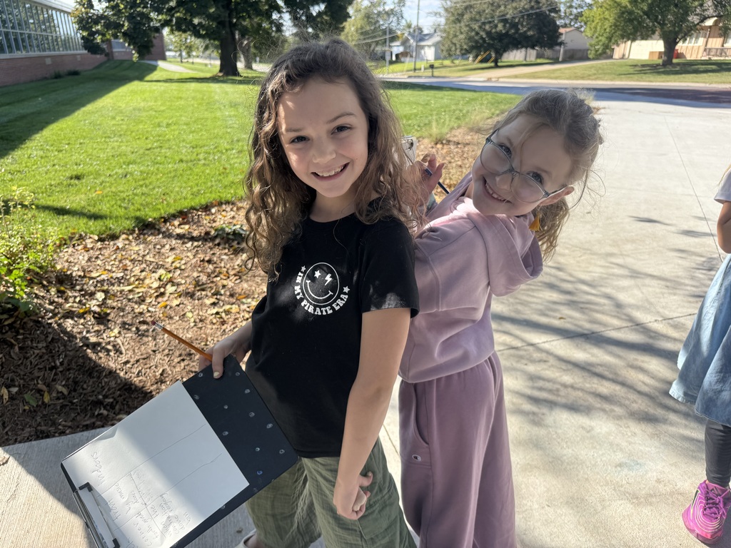 Two girls standing outside on cement with clipboards and papers in their hands.