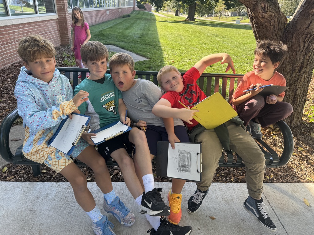 5 boys sitting on a bench with clipboards and papers in their hands.