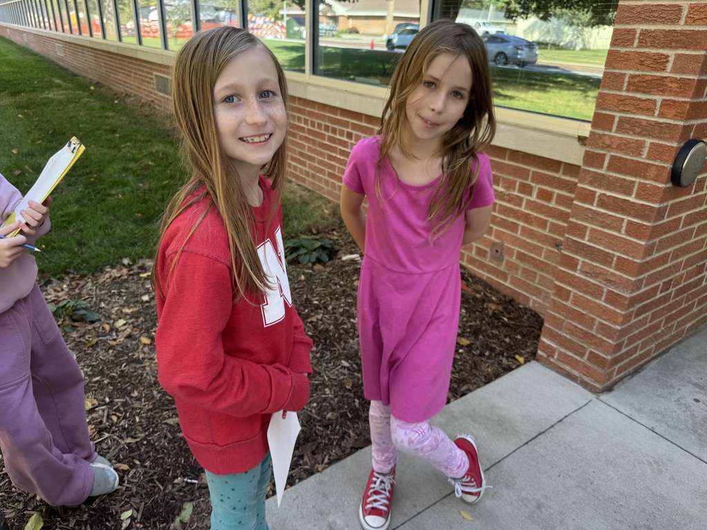 Two girls standing outside on cement with clipboards and papers in their hands.