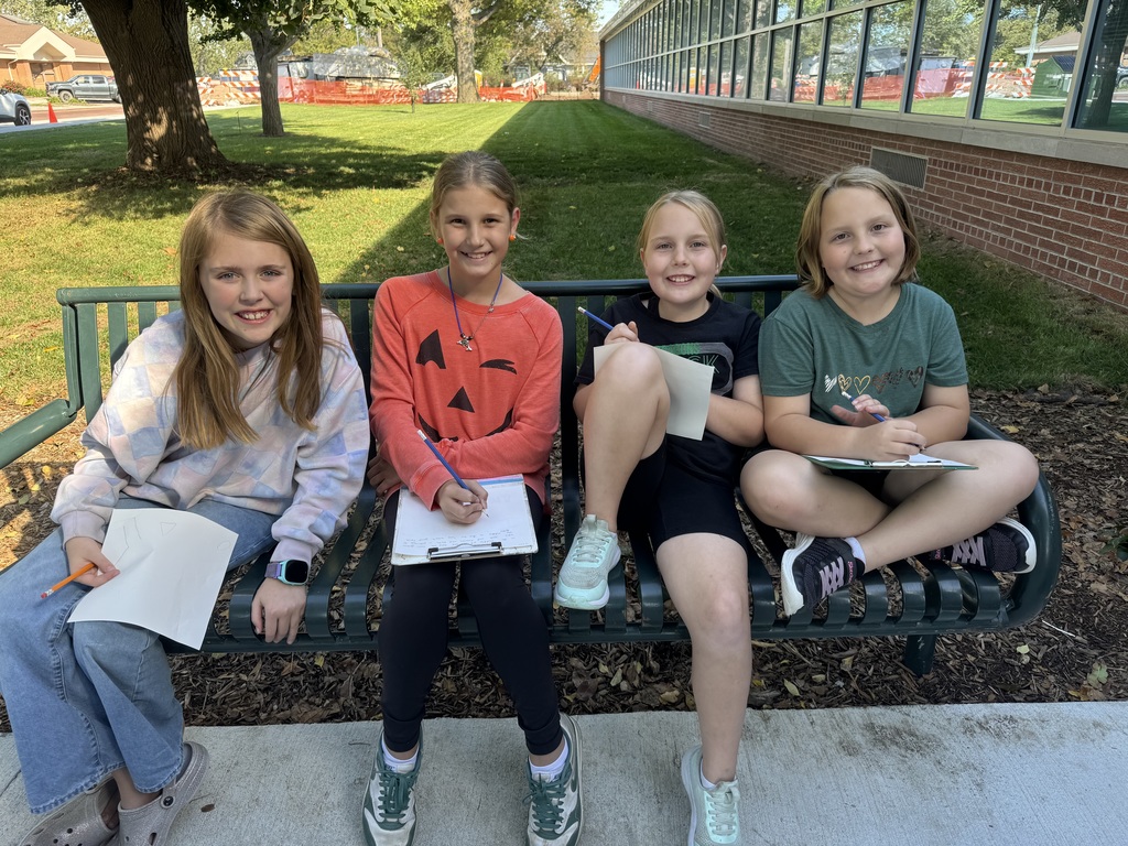 4 girls sitting on a bench with clipboards and papers in their hands.