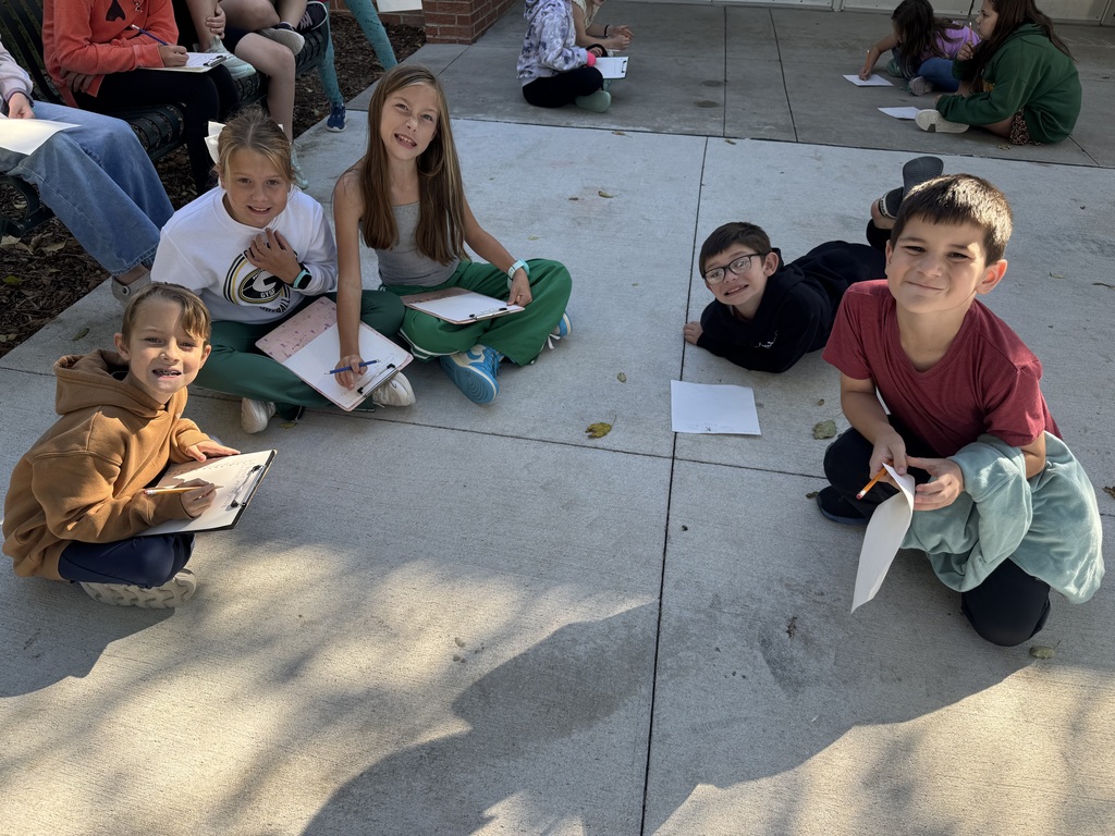Group of students sitting and laying outside on cement with clipboards and papers in their hands.