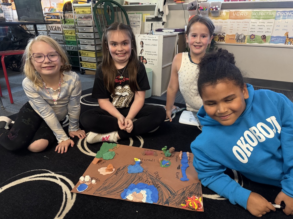 Group of girls sitting on carpet with clay made into animal landforms.