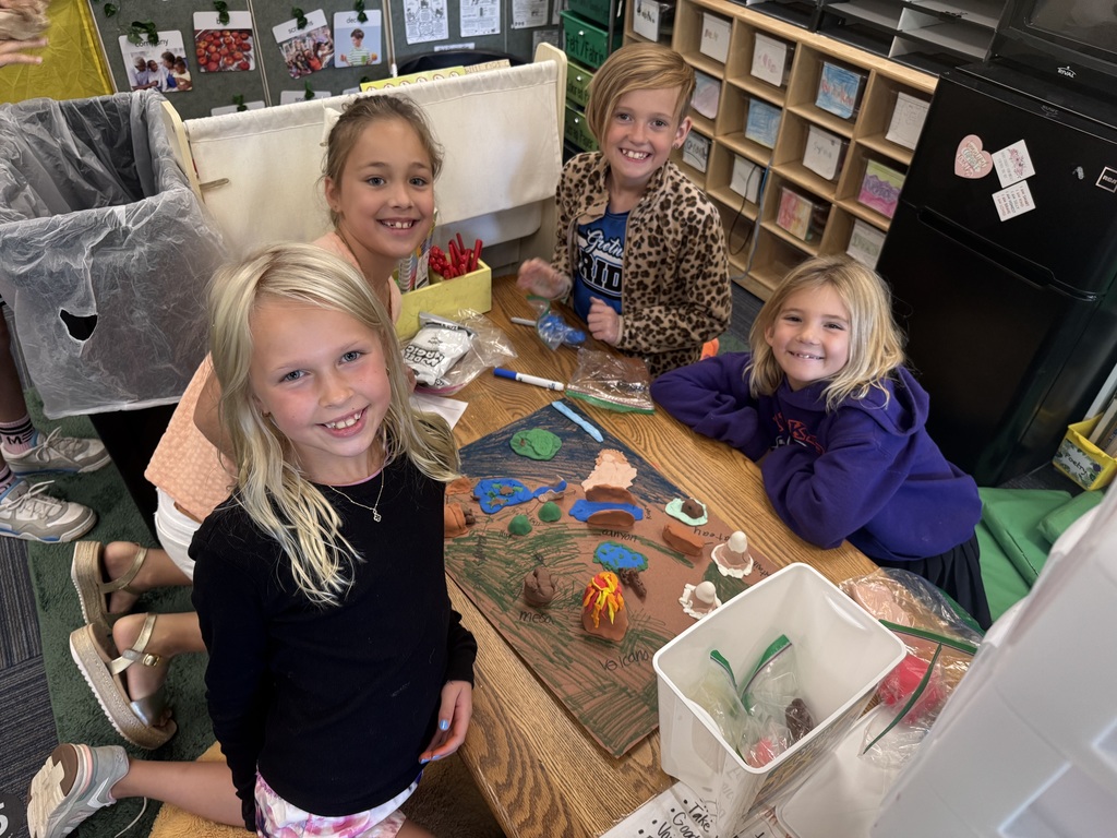 Group of girls sitting around a table with clay made into animal landforms.