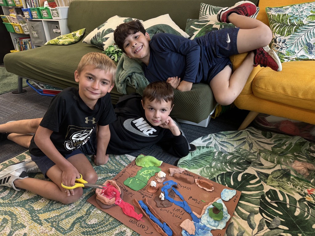 Group of boys sitting on carpet with clay made into animal landforms.
