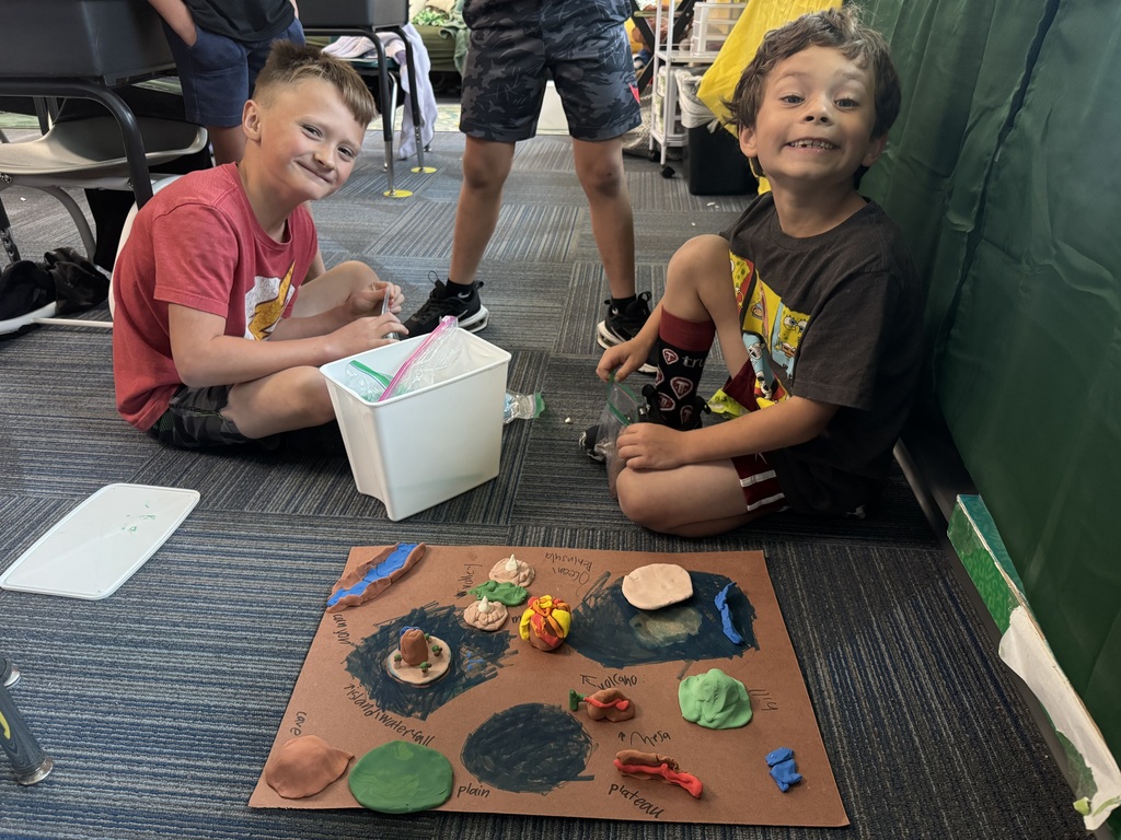 Group of boys sitting on carpet with clay made into animal landforms.