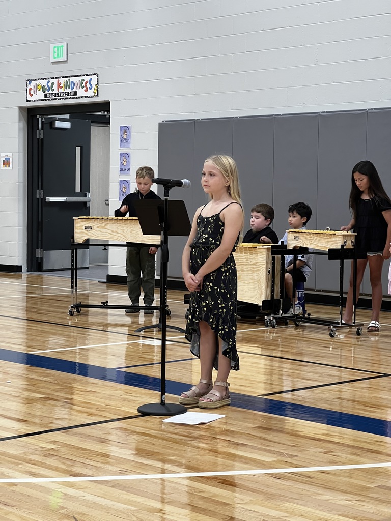 A 3rd grade student stands to sing her solo as four 3rd graders play the xylophone in the background.