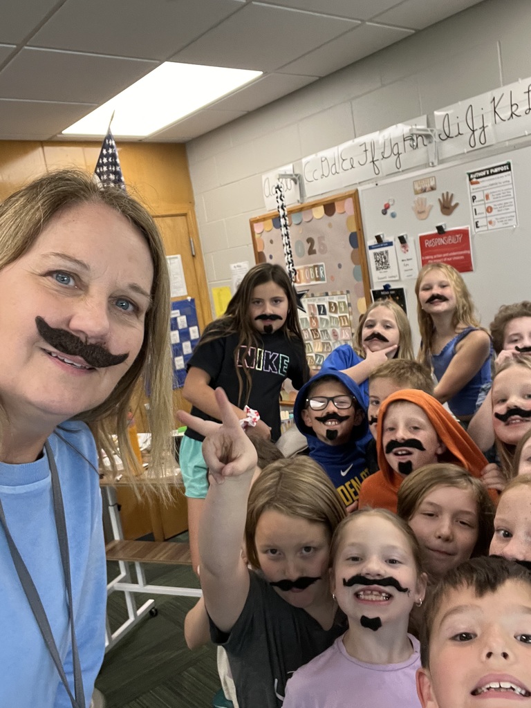 Teacher along with her students with most wearing fake mustaches.