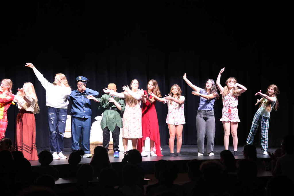 The cast of the one act all standing on the stage waving their arms. 
