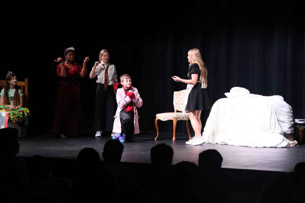 Students in the one act play. One male student is on his knees with three students behind him and one student in front of him. 