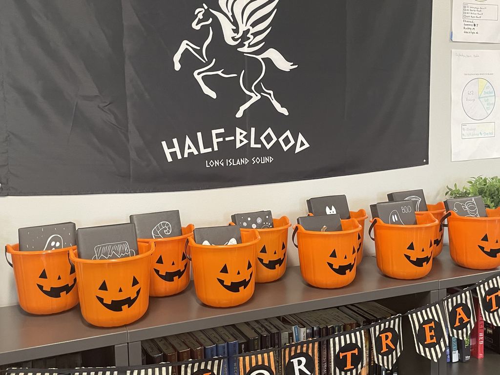 Pumpkin halloween buckets sit on a counter with books wrapped in black wrapping paper inside them. 