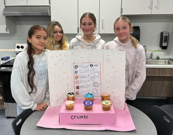 Four female students pose with a poster board and 6 cupcakes based on popular cookie types. 