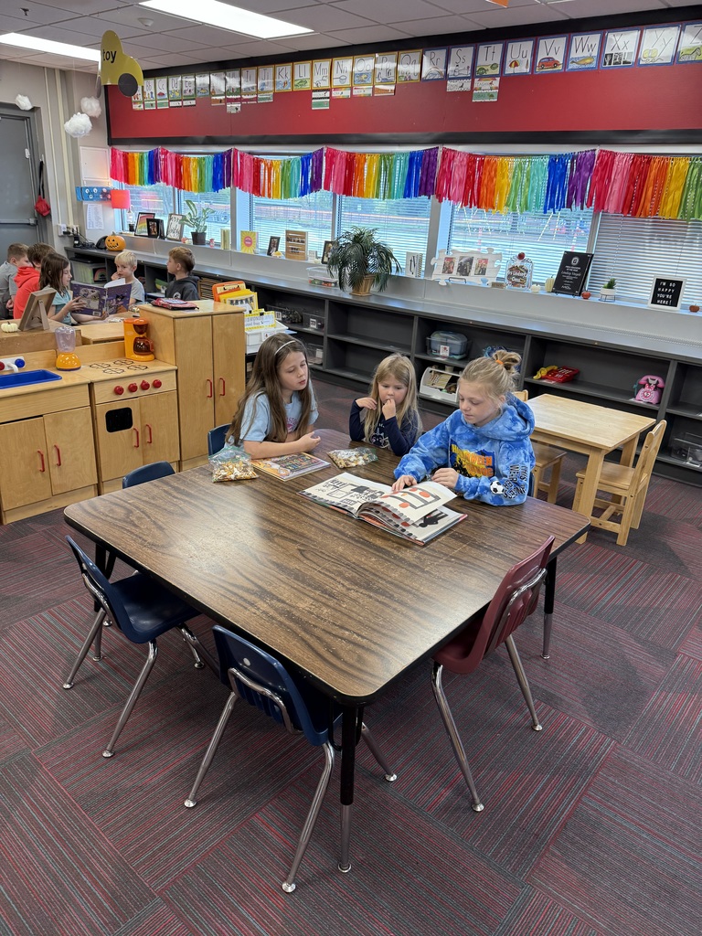 Three girls sitting a brown table reading a book.