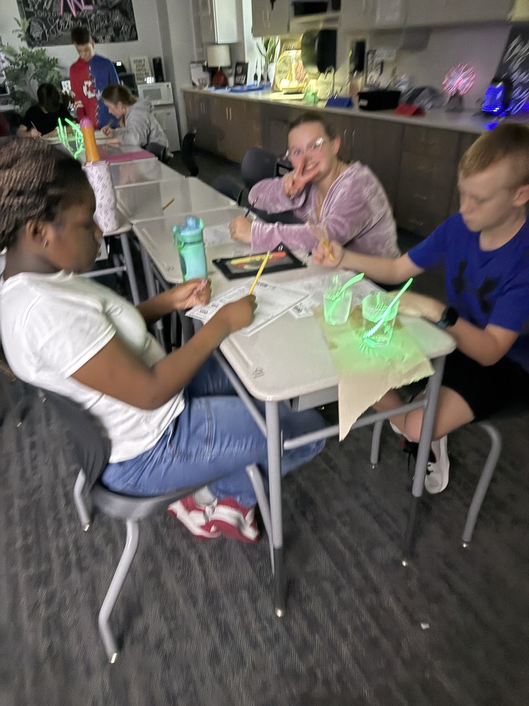 Students working at desks with a glowing item in a cup of liquid. They are taking notes. 