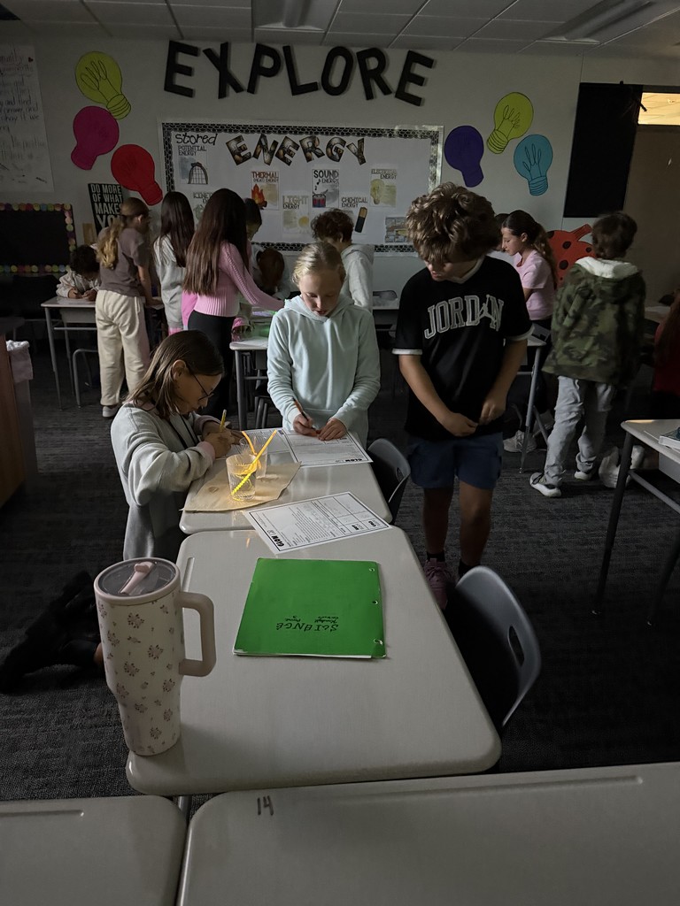 Students working at desks with a glowing item in a cup of liquid. They are taking notes. 