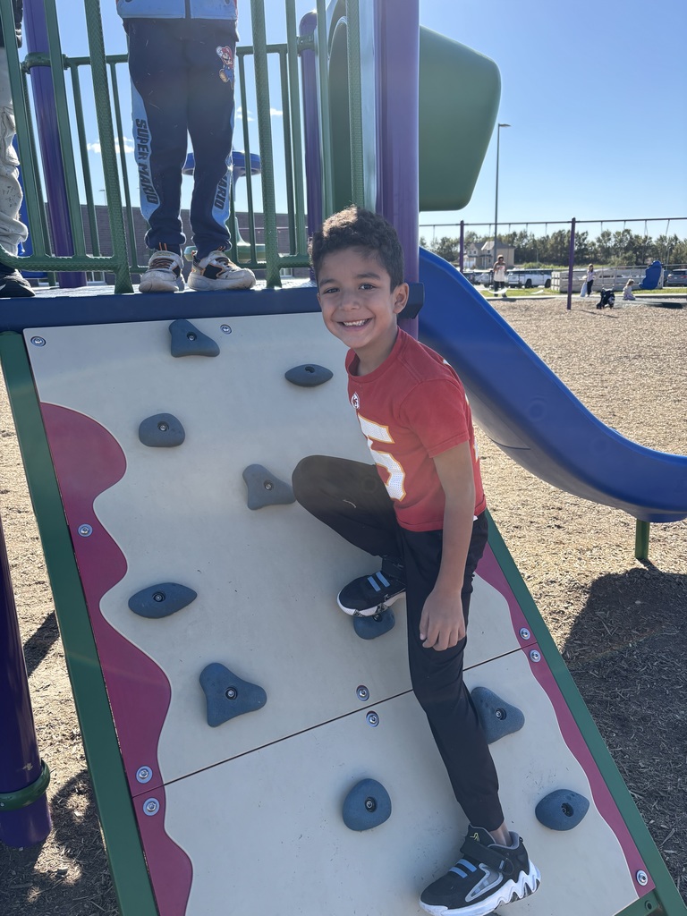 A first grade boy smiling climbing up the rock wall.