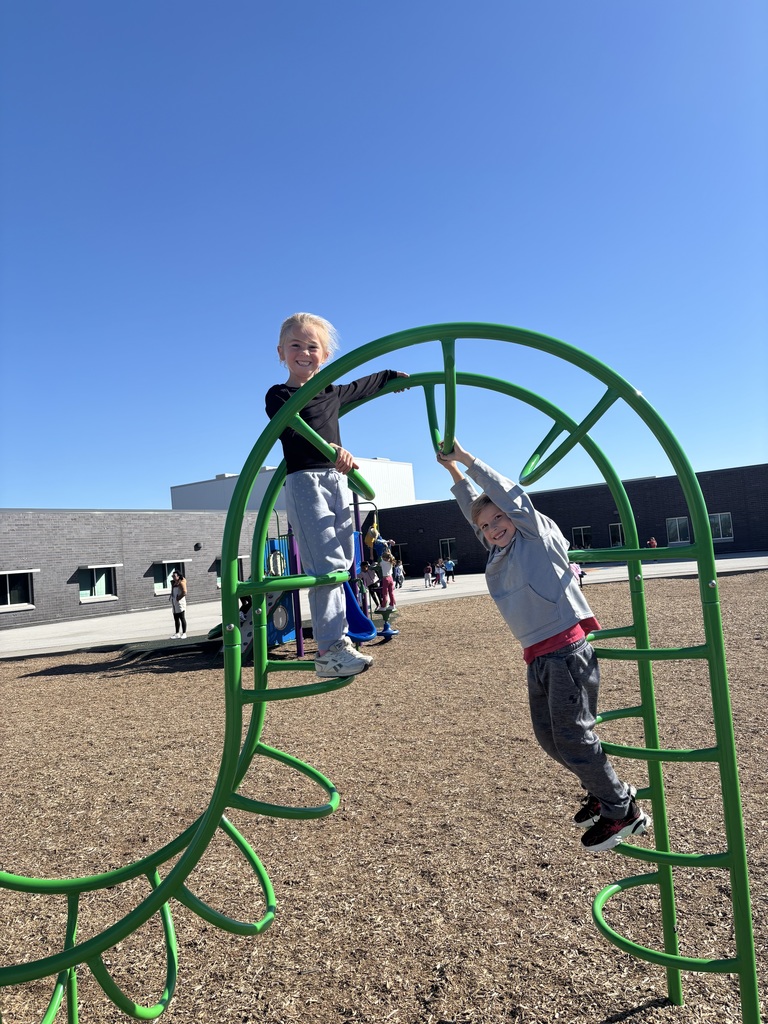 Two first graders climbing on a piece of playground equipment.