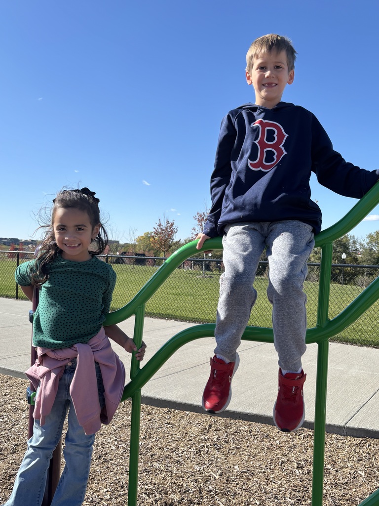 Two first graders standing or sitting on a piece of climbing equipment.