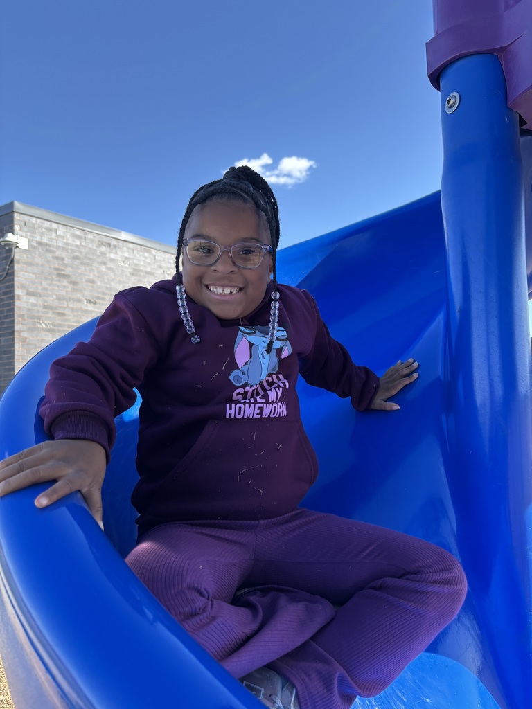 A first grade girl smiling going down a blue slide.