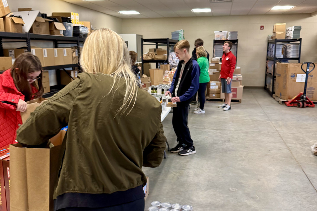staff and students surround tables filled with non perishable food items being filled in bags for community members in need