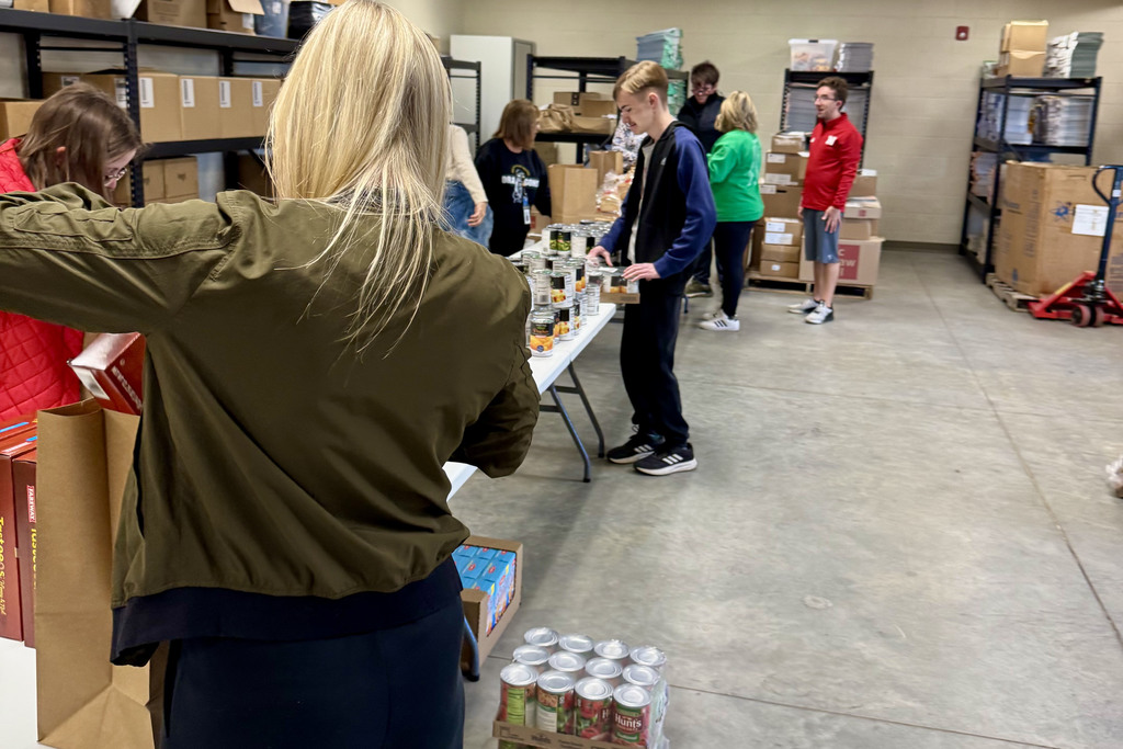 long tables filled with non perishable food items with students from the young adult program filling bags for community members in need