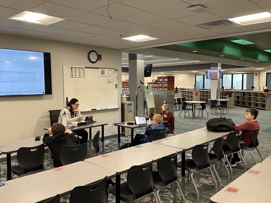Four students sit at desks with a teacher in the front of the room. 