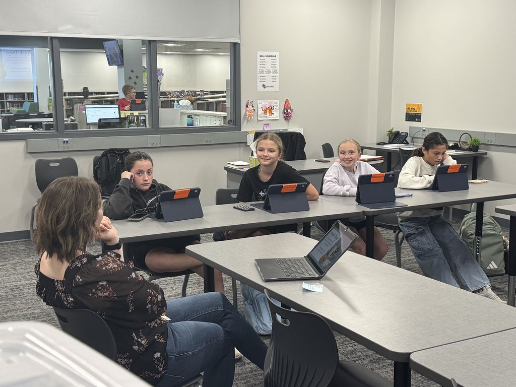 A teacher is working with four students. The students have iPads in front of them on the desks. 