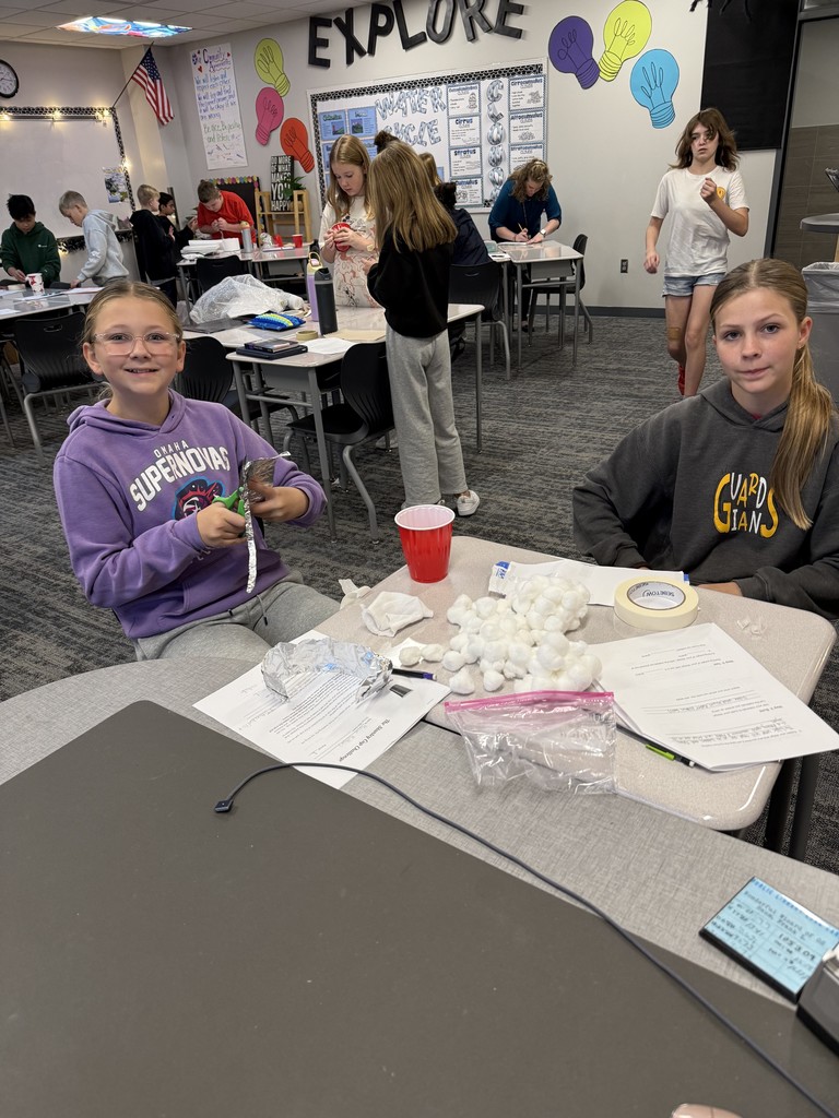 Students at desks working on cups. Kids in the background working at other tables. 
