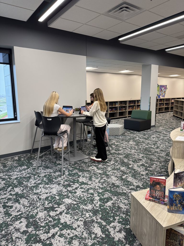 Three  students are working at a tall table with their iPads. 
