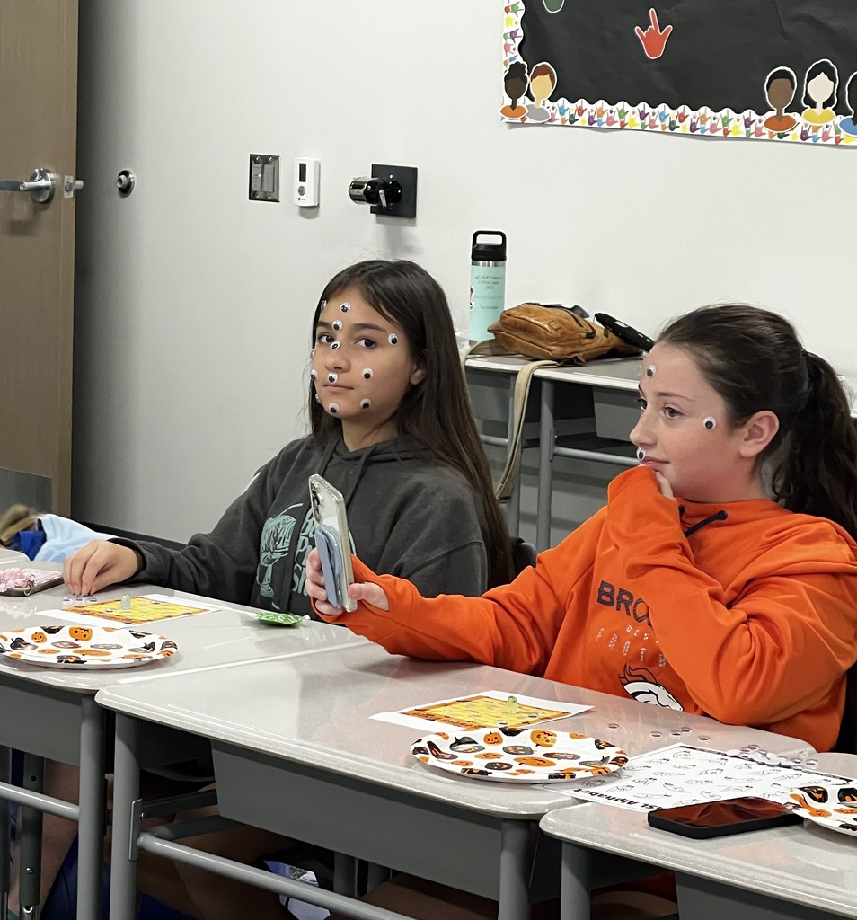 Two student sit at desks. They have googly eyes on their faces. 