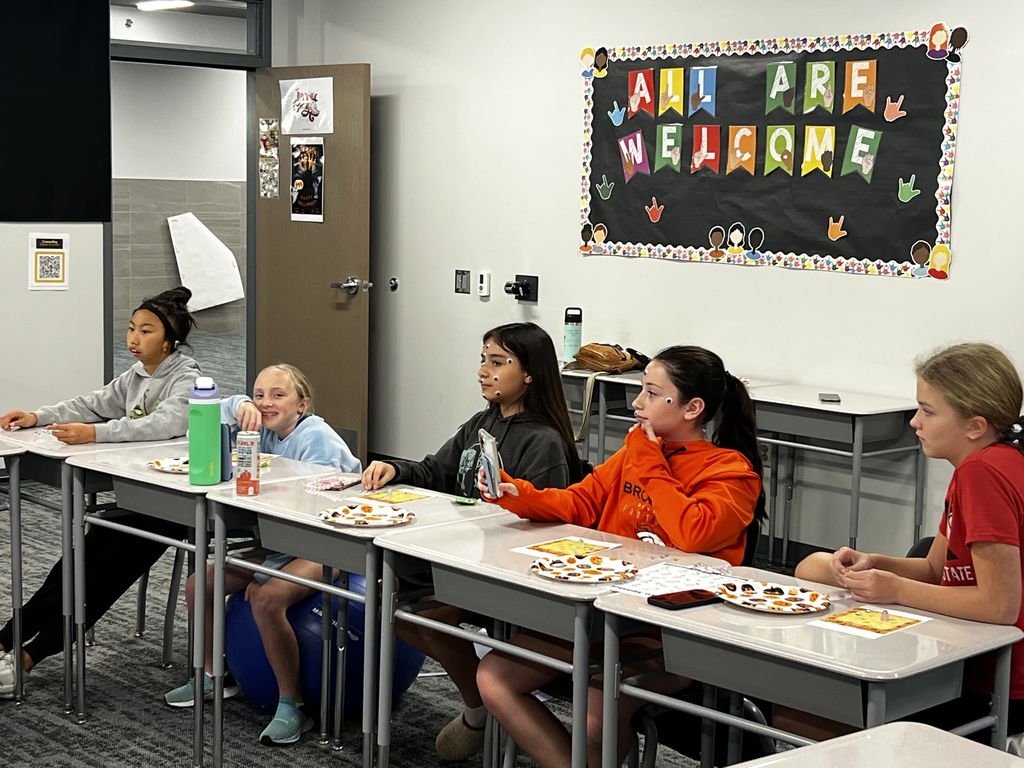 A group of five girls sit at desks. There are Halloween plats on their tables. 